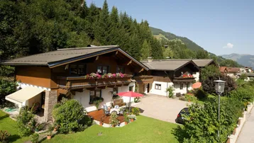 Traditionelles Alpenhaus mit Holzbalkonen, gepflegtem Garten und sonniger Terrasse mit Bergblick.