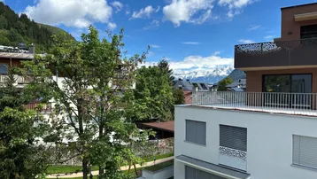 Panoramablick auf die Berge mit umliegenden Gebäuden und üppigem Grün unter blauem Himmel.