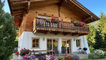 Charmantes Holzchalet mit blühendem Garten, Terrasse und Balkon, umgeben von grüner Natur.