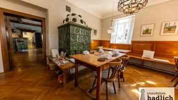 Gemütlicher Essbereich mit traditionellem Kachelofen, Holztischen und Bänken sowie Fischgrätparkettboden.