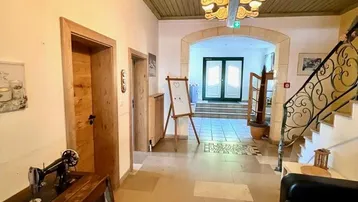 Geräumiger Eingangsbereich mit Steinfliesenboden, Holzdecke und einer geschwungenen Treppe, die in die oberen Etagen führt.