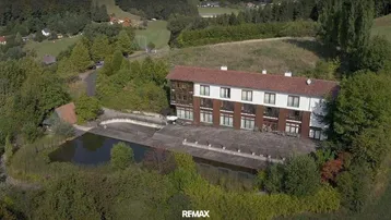 Luftaufnahme eines großen Gebäudes mit angrenzendem Teich und weitläufiger Grünfläche.