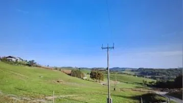 Weitläufige grüne Hügellandschaft mit Strommasten und einem Bauernhof in der Ferne unter blauem Himmel.