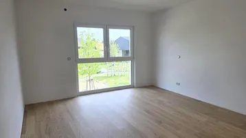 Helles Schlafzimmer mit großem Fenster und Blick ins Grüne, ausgestattet mit Parkettboden.