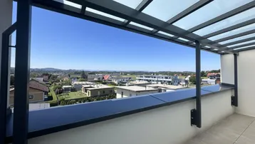 Überdachte Terrasse mit weitem Blick über die umliegende Wohngegend und grüne Hügel.