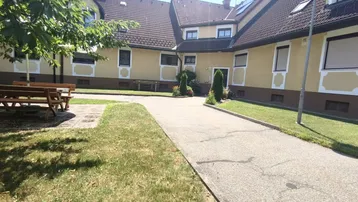 Mehrere Gebäude mit gelber Fassade, gepflastertem Weg und grünen Rasenflächen im Freien.
