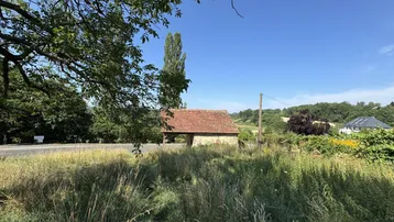 Altes Steingebäude mit Ziegeldach in ländlicher Umgebung unter blauem Himmel.