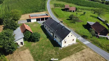 Luftaufnahme eines ländlichen Anwesens mit mehreren Gebäuden, umgeben von grünen Feldern und einer Straße.