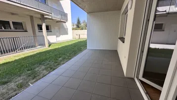 Geräumige geflieste Terrasse im Erdgeschoss mit direktem Zugang zu einer kleinen Rasenfläche.