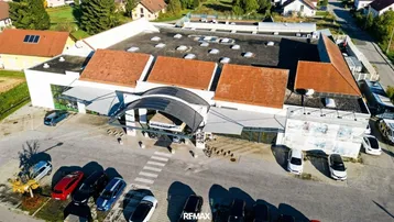 Luftaufnahme eines Gewerbegebäudes mit großem Parkplatz und umliegenden Wohnhäusern in einer städtischen Umgebung.