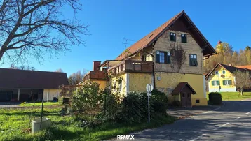 Gelbes Haus mit Holzbalkonen und Satteldach in ländlicher Umgebung unter blauem Himmel.