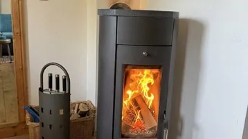Nahaufnahme eines modernen Holzofens mit brennendem Feuer, der Wärme und Gemütlichkeit spendet.