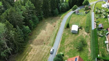 Luftaufnahme eines Grundstücks mit angrenzendem Wald und einer Zufahrtsstraße in ländlicher Umgebung.