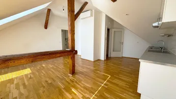Helles Dachgeschosszimmer mit sichtbaren Holzbalken, Parkettboden und einer integrierten Küchenzeile.