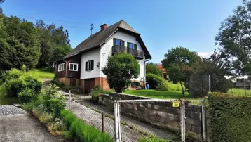 Ländliches Einfamilienhaus mit Satteldach und Balkon, umgeben von viel Grün und einer Zufahrt.