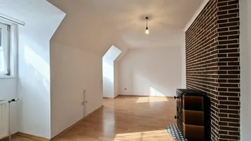 Ein geräumiges Wohnzimmer mit Laminatboden, Dachschrägen und einem traditionellen Kachelofen an der Ziegelwand.