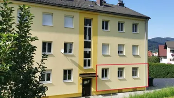 Mehrfamilienhaus mit gelber Fassade, vielen Fenstern und grüner Umgebung.
