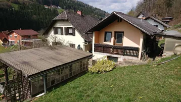 Mehrere Häuser in einer ländlichen Umgebung mit grünen Hügeln und bewaldeten Hängen.