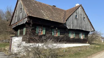 Traditionelles Holzhaus mit Satteldach und grünen Fensterläden in ländlicher Umgebung.
