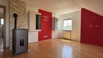 Wohnzimmer mit Holzboden, Kaminofen und roten Akzentwänden unter der Dachschräge.