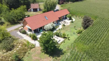 Luftaufnahme eines Einfamilienhauses mit rotem Ziegeldach, umgeben von grünen Feldern und Bäumen.