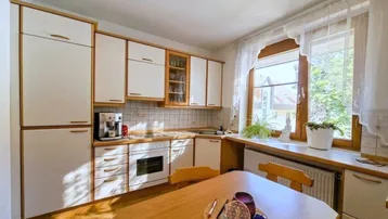 Gemütliche Küche mit weißen Schränken, Holzakzenten, Esstisch und Fenster mit viel Tageslicht.