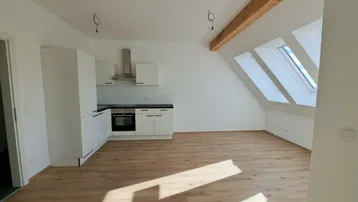Offener Wohnbereich mit integrierter Küche, Dachschrägen, Holzbalken und viel Tageslicht durch Dachfenster.