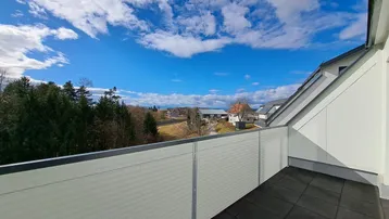 Geräumiger Balkon mit weitem Blick über die Landschaft und die umliegenden Häuser unter blauem Himmel.