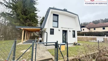 Modernes Einfamilienhaus mit weißer Fassade und dunklem Dach in ländlicher Umgebung.