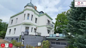 Elegante Villa mit markanter Architektur, Balkonen und einer Garage im Untergeschoss, umgeben von Grün.