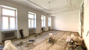 Großes Wohnzimmer im Rohzustand mit hohen Decken und Stuckverzierungen, bereit zur Renovierung.