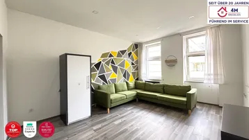 Helles Wohnzimmer mit modernem Design, grüner Couch, geometrischer Wandgestaltung und Holzboden.