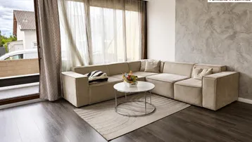 Helles Wohnzimmer mit beigem Ecksofa, dunklem Holzboden und Zugang zum Balkon.