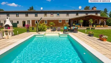 Großer Außenbereich mit Swimmingpool, Grillplatz und einer überdachten Terrasse vor dem Gebäude.