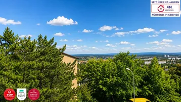 Weitläufiger Blick über die Stadt und grüne Baumwipfel unter blauem Himmel.