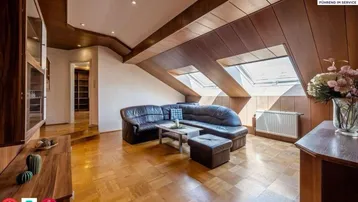 Gemütliches Wohnzimmer im Dachgeschoss mit Holzbalken, Parkettboden und Dachfenstern, die viel Licht hereinlassen.