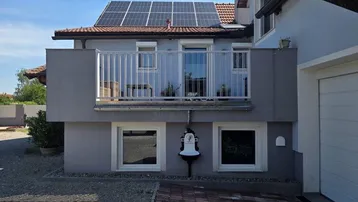 Fassade des Hauses mit einem Balkon im Obergeschoss und Photovoltaikanlage auf dem Dach.