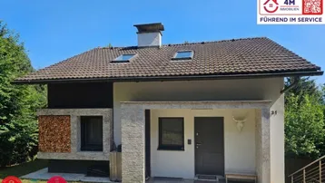 Modernes Einfamilienhaus mit Satteldach, dekorativem Holzstapel und steinverkleidetem Eingang.
