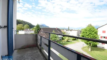Balkon mit Bergblick und weitem Ausblick über die Dächer der Umgebung unter blauem Himmel.