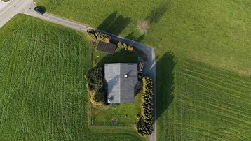 Luftaufnahme eines Einfamilienhauses umgeben von grünen Wiesen und einer Zufahrtsstraße.
