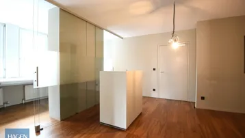 Moderner Büroraum mit Holzboden, Glasabtrennung und einem zentralen Arbeitstisch, der vielseitig nutzbar ist.