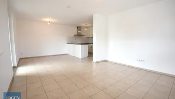 Helles, offenes Wohnzimmer mit integrierter Küchenzeile und Fliesenboden.