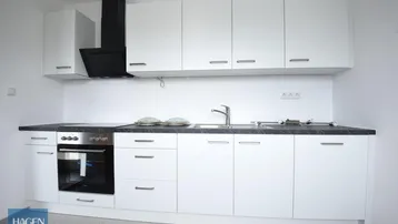 Moderne Einbauküche in Weiß mit dunkler Arbeitsplatte, ausgestattet mit Backofen und Induktionskochfeld.