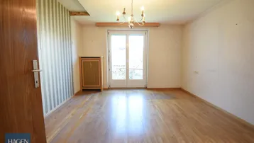 Zimmer mit Parkettboden, Kronleuchter und Zugang zu einem französischen Balkon.