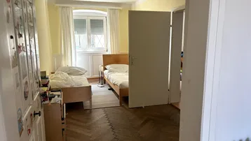 Schlafzimmer mit zwei Betten, Parkettboden und Fenster mit Blick ins Grüne.