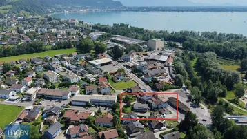 Luftaufnahme einer Stadt am See mit Bergen im Hintergrund, das Grundstück ist rot markiert.