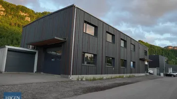 Modernes Geschäftsgebäude mit dunkler Holzfassade und großen Fenstern vor einer bergigen Landschaft.