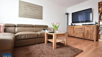 Gemütliches Wohnzimmer mit beigem Ledersofa, Holzboden und modernem TV-Möbel.
