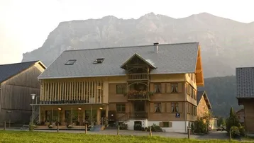 Traditionelles Gebäude mit Holzfassade und modernem Anbau vor einer beeindruckenden Bergkulisse.