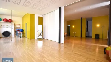 Großer, heller Raum mit Holzboden und gelben Wänden, ausgestattet für Fitness- oder Therapiezwecke.